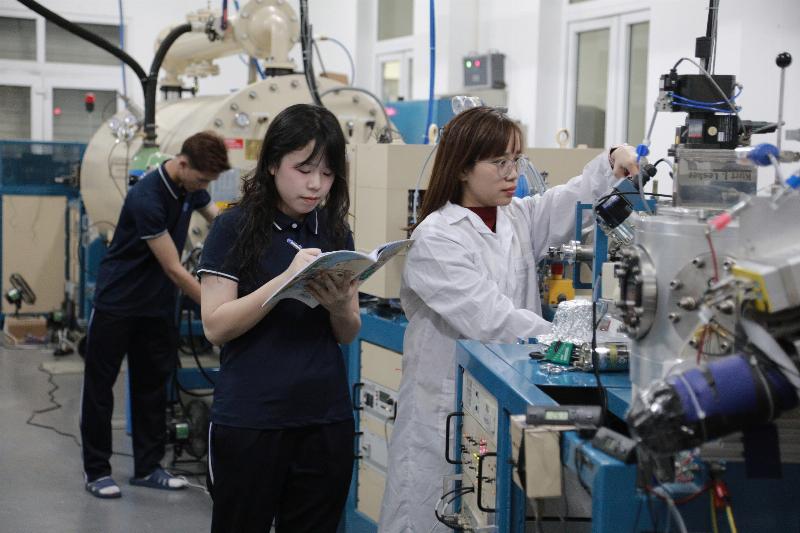 Hình ảnh sinh viên thực tập đang xem sơ đồ mạch hoặc thiết bị, liên hệ kiến thức lý thuyết mạch với thực tế