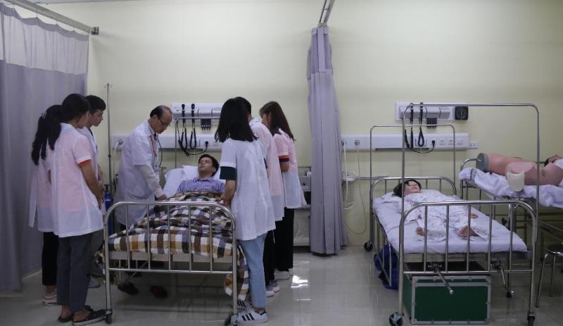 Một sinh viên y khoa đang thực hành kỹ năng nghe tim phổi trên mô hình hoặc bạn học, dưới sự hướng dẫn của giảng viên.